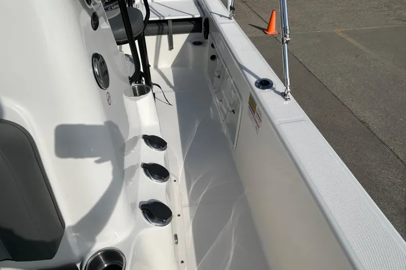 Slide: The Image of 2026 Sundance DX22 boat interior with rod holders and seating, docked on pavement. - 24