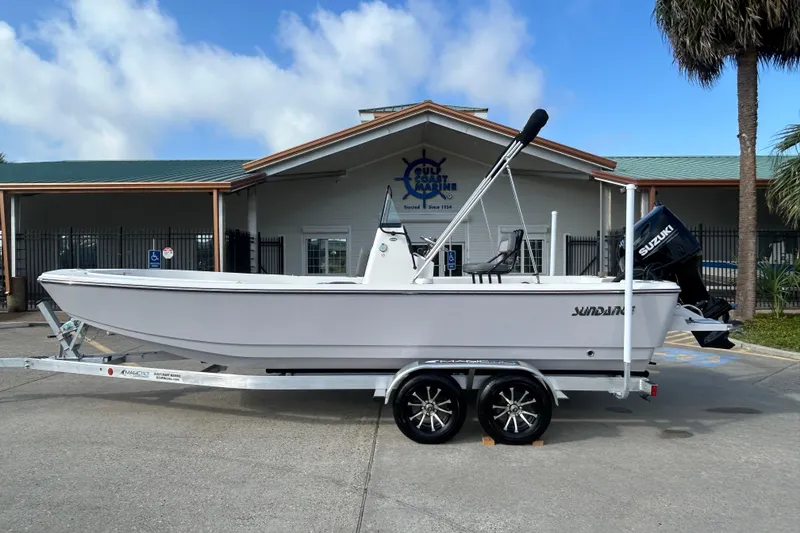 Slide: The Image of 2026 Sundance DX22 boat on trailer, parked outside a marine dealership. - 7