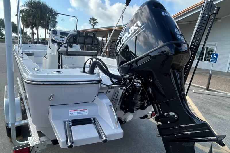 Slide: The Image of 2026 Sundance DX22 boat with Suzuki outboard motor, parked near palm trees and a building. - 9