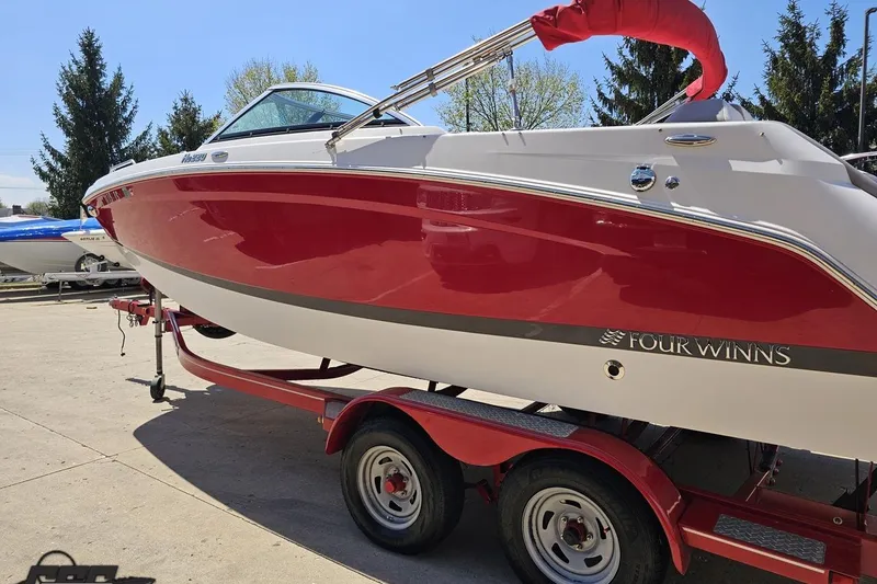 Slide: The Image of 2018 Four Winns HD220 boat in vibrant red on a trailer, parked outdoors. - 29