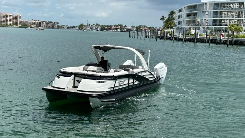 Slide: The Image of 2024 Bennington QX Line boat cruising on a scenic waterfront with modern buildings in the background. - 2