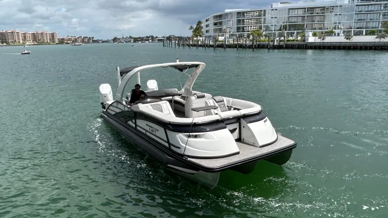 Slide: The Image of 2024 Bennington QX Line boat cruising on a calm waterway near modern buildings. - 4