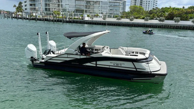 Slide: The Image of 2024 Bennington QX Line luxury pontoon boat on water near modern buildings. - 5