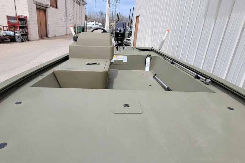 Slide: The Image of 2017 Tracker Grizzly 1648 SC boat, olive green, parked outdoors near industrial buildings. - 14