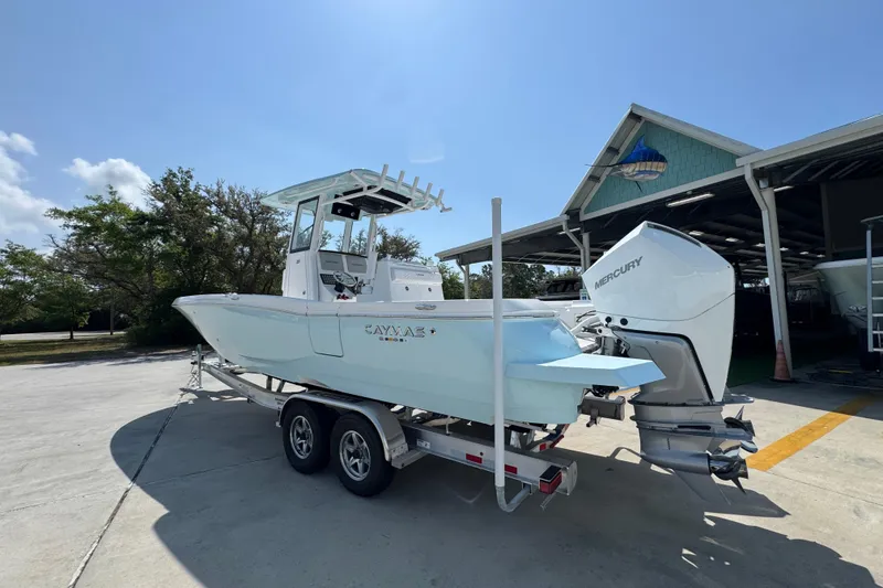 Slide: The Image of 2026 Caymas 291 boat on trailer with Mercury engine, parked outdoors near a boathouse. - 16