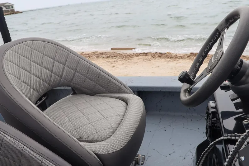 Slide: The Image of 2025 Haynie 24 High Output boat interior with steering wheel and quilted seat by the shore. - 31