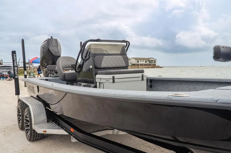 Slide: The Image of 2025 Haynie 24 High Output boat on trailer by the waterfront, under cloudy skies. - 4