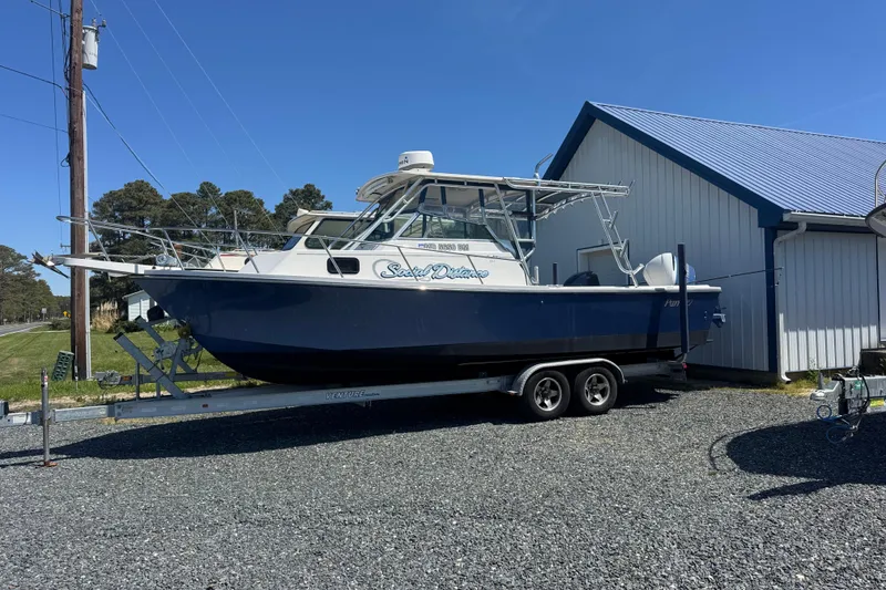 The Image of 2002 Parker 2510 Walkaround boat on trailer beside a blue-roofed building. - 0