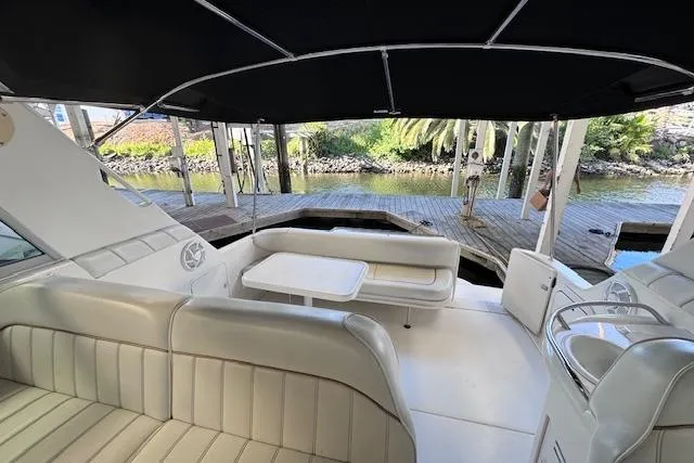 Slide: The Image of 1998 Sea Ray Sundancer 330 interior with seating and table, docked by a scenic waterfront. - 11