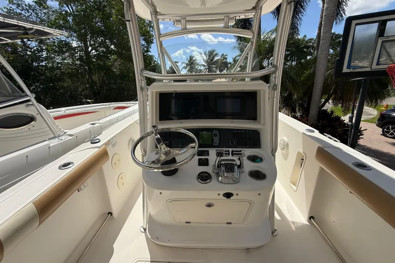 Slide: The Image of 2007 Boston Whaler 270 Outrage boat console with steering wheel and controls, surrounded by lush greenery. - 52