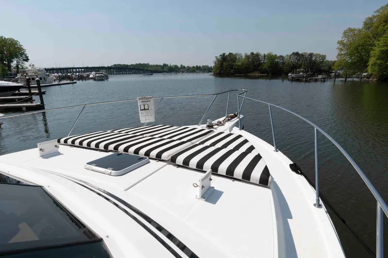Slide: The Image of 1999 West Bay 58 Sonship Pilothouse yacht with striped sunbed on deck, surrounded by serene water and trees. - 15