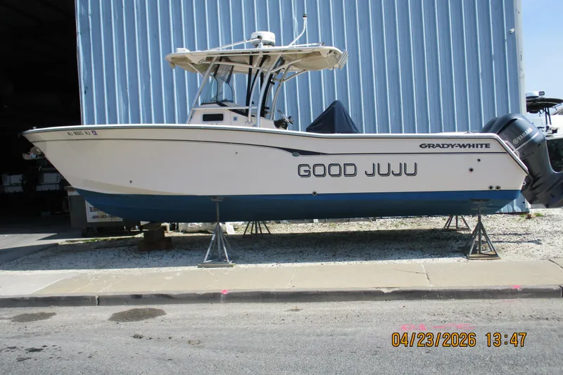 The Image of 2007 Grady-White Bimini 306 boat named "Good Juju" on stands outside a blue building. - 0