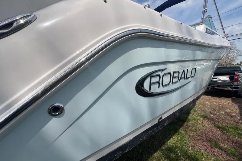 Slide: The Image of 2022 Robalo R227 Dual Console boat side view with logo, parked outdoors. - 58
