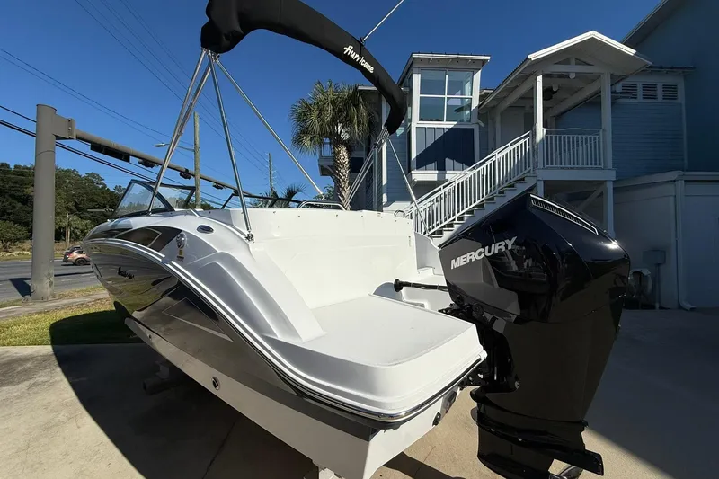 Slide: The Image of 2025 Hurricane SunDeck 235 OB boat with Mercury outboard engine, parked near a coastal home. - 3