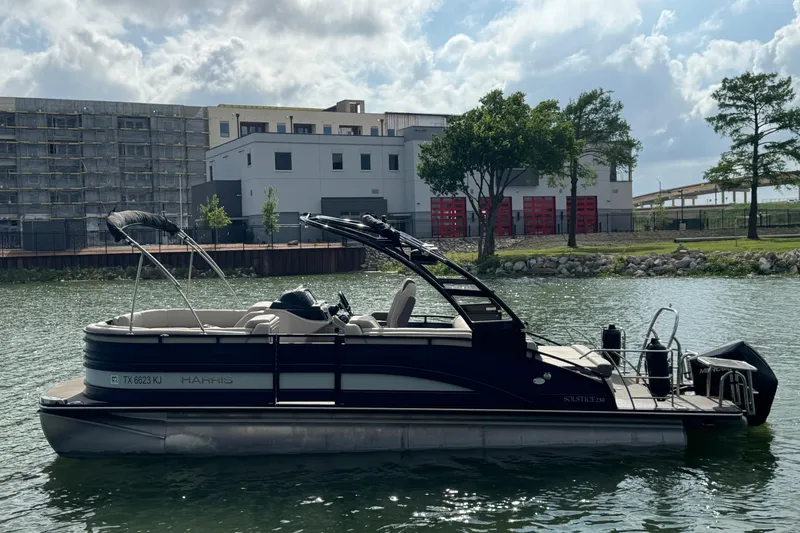 The Image of 2021 Harris Solstice 230 pontoon boat on a calm river with urban backdrop. - 1