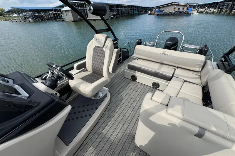 Slide: The Image of 2021 Harris Solstice 230 pontoon boat interior with luxurious seating and helm, docked by the water. - 10