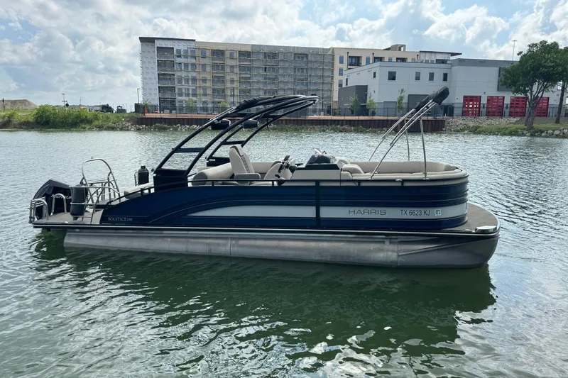 Slide: The Image of 2021 Harris Solstice 230 pontoon boat on a calm lake with buildings in the background. - 3