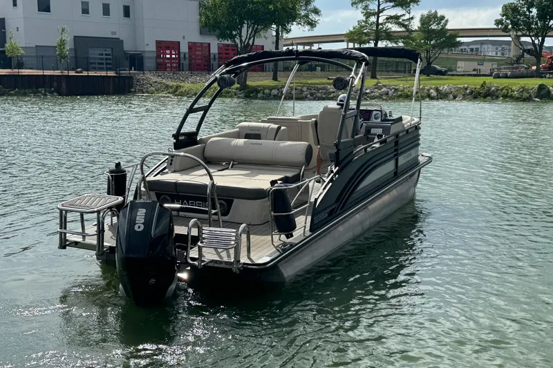 Slide: The Image of 2021 Harris Solstice 230 pontoon boat on a calm lake near a modern building. - 5
