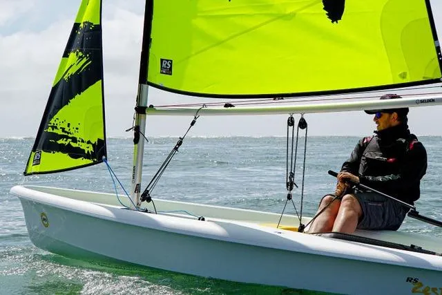 Slide: The Image of 2021 RS SAILING Zest sailboat with vibrant yellow sails on open water. - 2