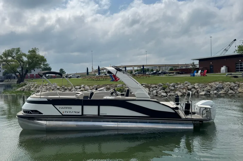 The Image of 2023 Harris Grand Mariner 250 pontoon boat on calm water near a rocky shoreline. - 1
