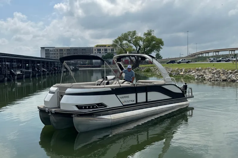 Slide: The Image of 2023 Harris Grand Mariner 250 pontoon boat on a calm lake near a marina. - 3