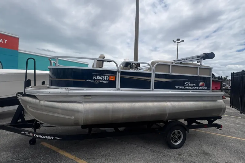 Slide: The Image of 2022 Sun Tracker Bass Buggy 16 XL Select pontoon boat on trailer, parked outdoors. - 4
