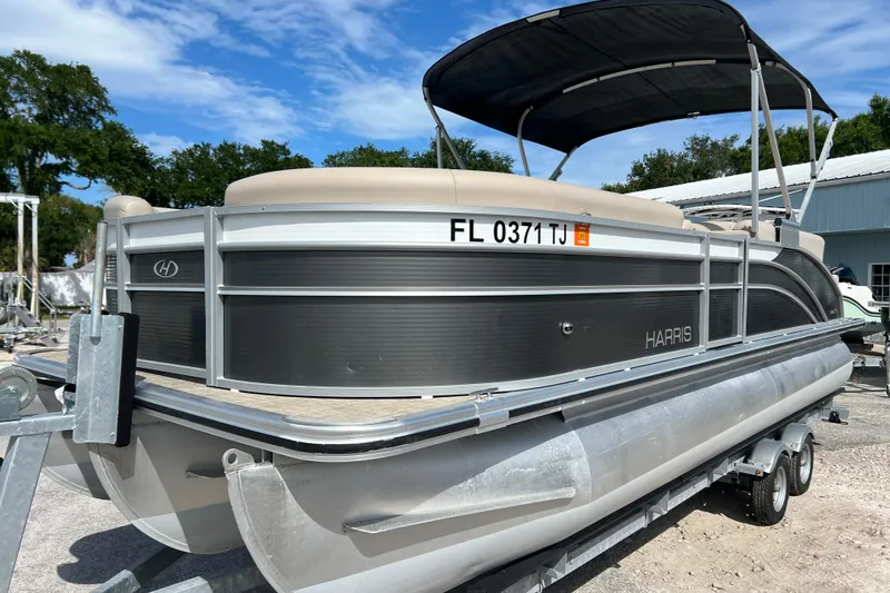 Slide: The Image of 2023 Harris Cruiser 230 pontoon boat on trailer, under blue sky. - 4