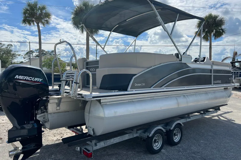 Slide: The Image of 2023 Harris Cruiser 230 pontoon boat with Mercury engine on trailer, under sunny skies. - 8