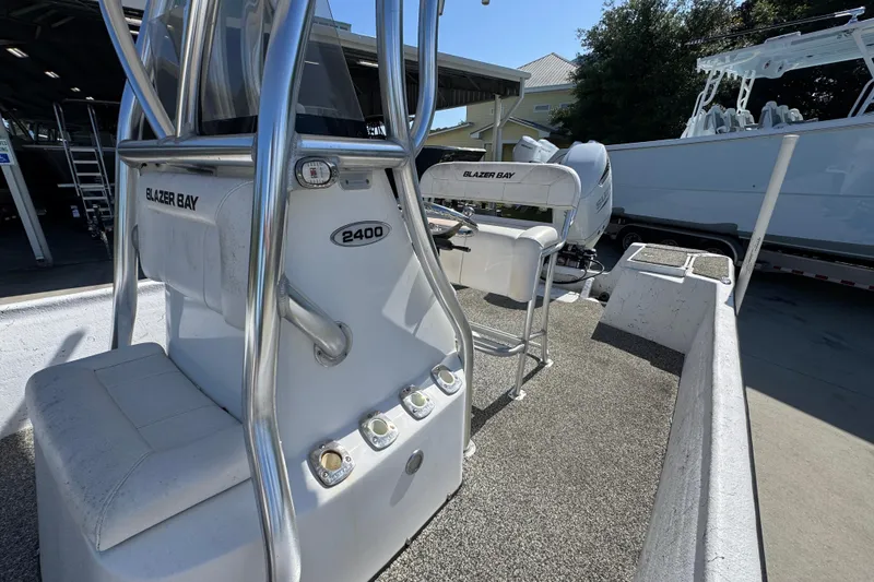 Slide: The Image of 2021 Blazer Bay 2400 boat interior with seating and controls, parked outdoors. - 26