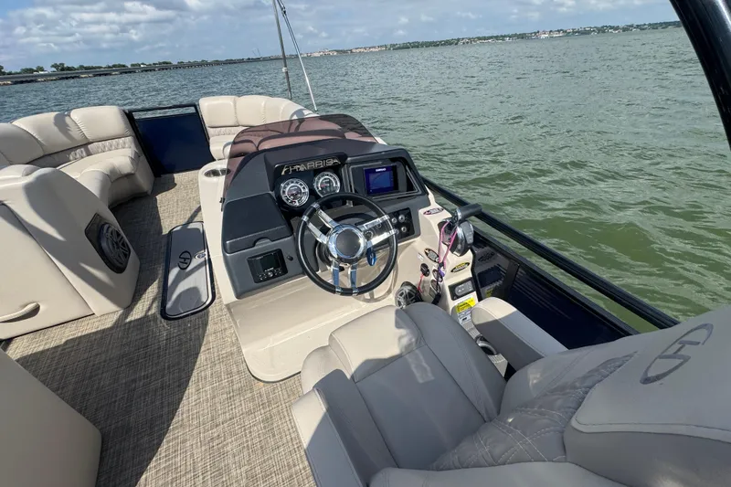 Slide: The Image of 2019 Harris Solstice 220 boat interior with steering wheel, dashboard, and seating on a lake. - 15