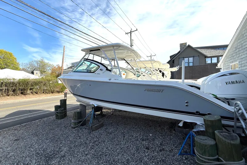Slide: The Image of 2026 Pursuit DC 266 Dual Console boat parked on gravel. - 2