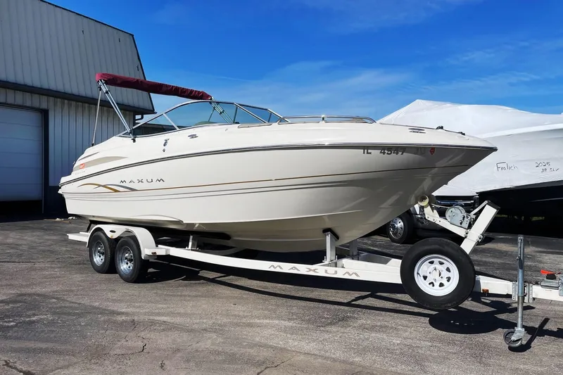 The Image of 2001 Maxum 2300 SR boat on trailer, parked outdoors under clear blue sky. - 0