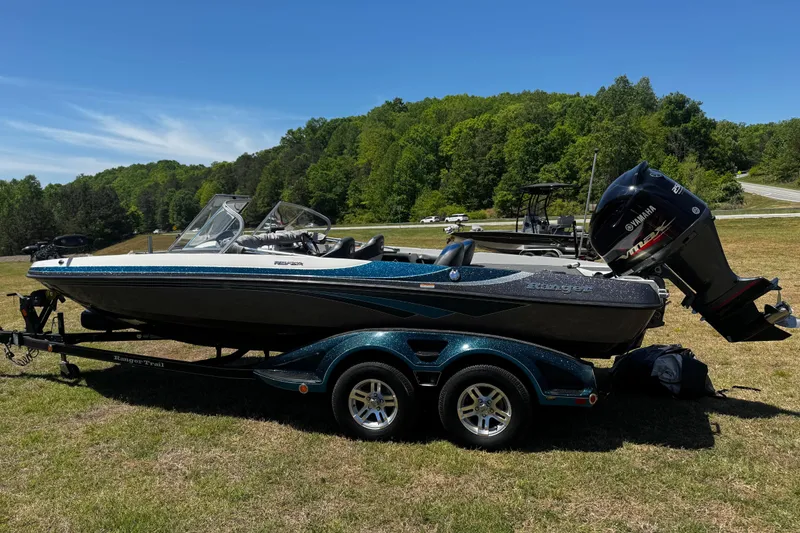 Slide: The Image of 2018 Ranger 212LS Reata boat on trailer, parked on grassy area with trees in background. - 3