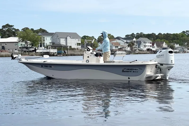 The Image of 2025 Carolina Skiff 21LS boat on water, with person steering, houses in background. - 1