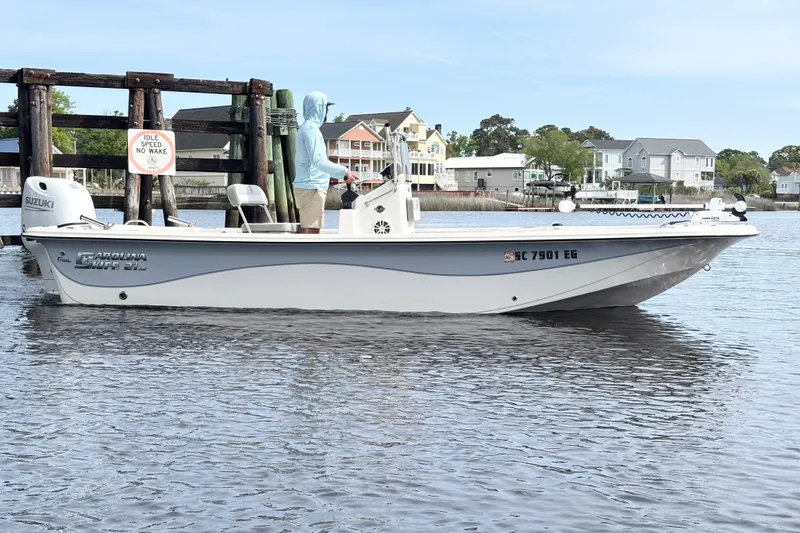 Slide: The Image of 2025 Carolina Skiff 21LS boat on calm water near dock, houses in background. - 4