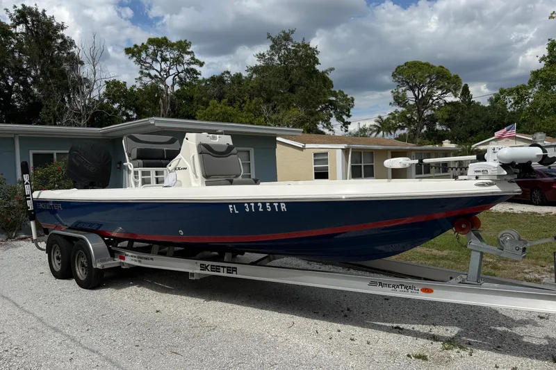 The Image of 2023 Skeeter SX230 boat on trailer, parked in residential driveway, under cloudy sky. - 0