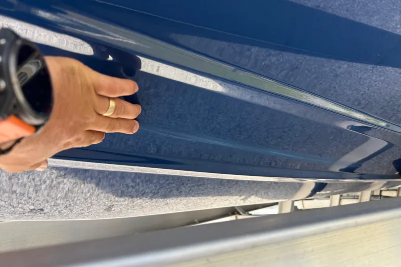 Slide: The Image of Hand inspecting the sleek blue hull of a 2023 Skeeter SX230 boat. - 7