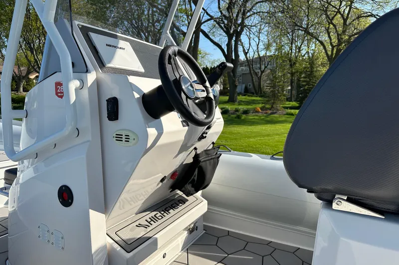 Slide: The Image of 2024 Highfield Sport 660 boat interior with steering wheel and seating, surrounded by greenery. - 7