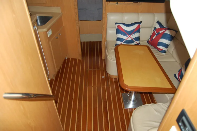 Slide: The Image of 2004 Tiara Yachts 3500 Open interior with wood flooring, cushioned seating, and nautical-themed pillows. - 8