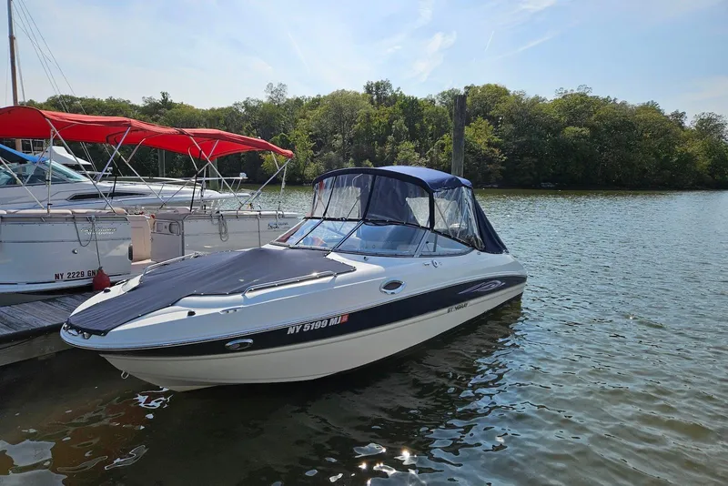 The Image of 2013 Stingray 234 LR boat docked on a calm lake with trees in the background. - 0
