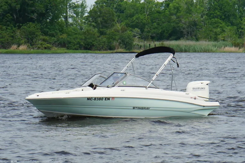 The Image of 2020 Stingray 191 DC boat with Suzuki engine on a lake, surrounded by greenery. - 0