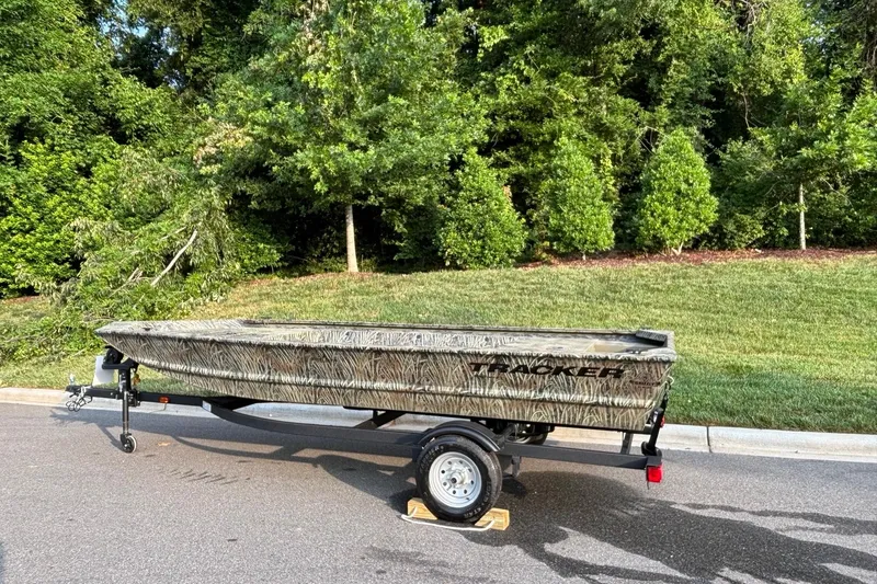 Slide: The Image of 2026 Tracker Grizzly 1648 Utility boat on trailer, parked on a road with greenery background. - 2