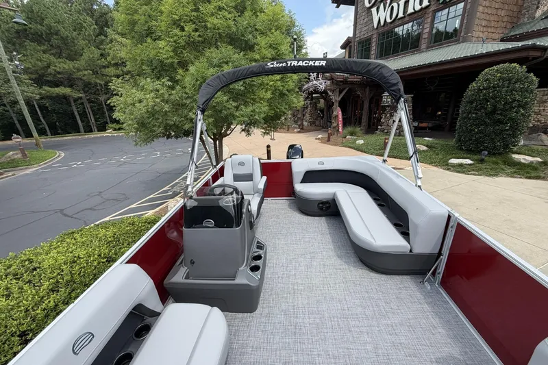 Slide: The Image of 2026 Sun Tracker Party Barge 16 DLX pontoon boat with seating, parked near a building. - 5