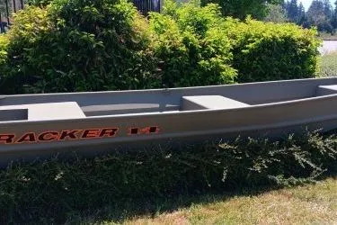 Slide: The Image of 2026 Tracker Grizzly 14 Jon boat displayed outdoors near greenery. - 2