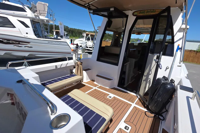 Slide: The Image of 2025 Ranger Tugs R-25 boat interior with seating and wooden deck, docked near other boats. - 12