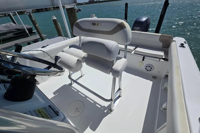 Slide: The Image of 2012 Sea Hunt Ultra 225 boat interior with steering wheel and seating, docked by the water. - 18
