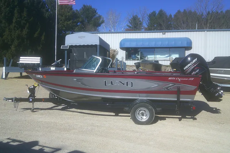 The Image of 2017 Lund 1875 Crossover XS boat on trailer, parked outdoors near a building. - 1