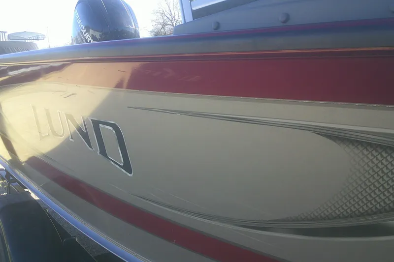 Slide: The Image of 2017 Lund 1875 Crossover XS boat with red and gray detailing, featuring a Mercury engine. - 25