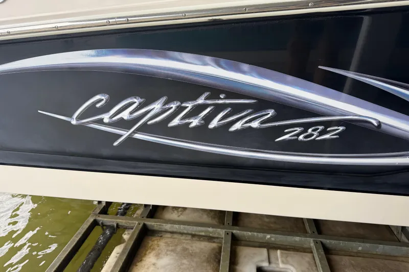 Slide: The Image of 2006 Rinker 282 Captiva Bowrider boat logo on hull, docked by water. - 22