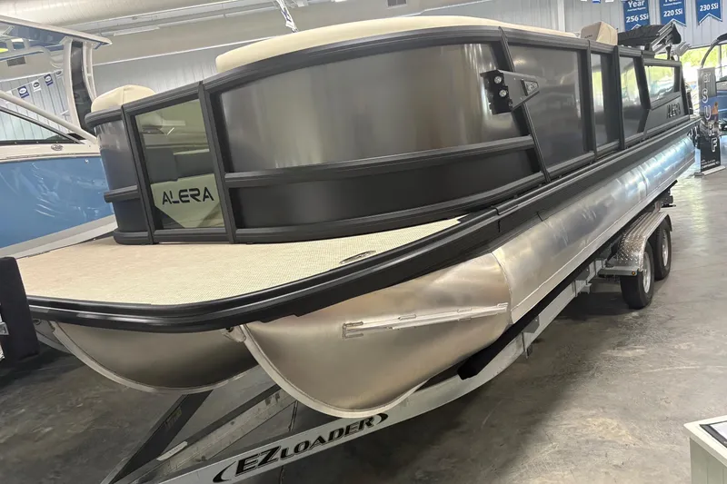 Slide: The Image of 2026 Alera M25Q pontoon boat on EZ Loader trailer in showroom. - 2